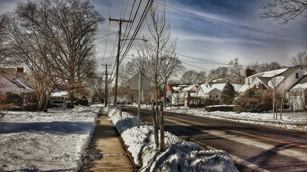 A snow-covered street in a suburban neighborhood after a winter storm, with downed power lines and trees blocking roads. The sky is overcast, and the scene is quiet and still, conveying a sense of isolation and disruption caused by the storm.