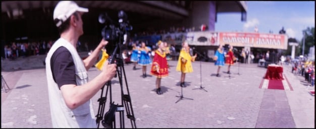 A split-screen image. On one side, a crowd of people at a traditional music festival, enjoying the live music in a field. On the other side, a person at home wearing a VR headset, fully immersed in a virtual concert experience with realistic visuals.