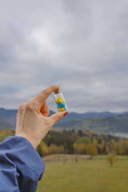 A person's hand holding a small bottle of vitamin D supplements, with a clear blue sky and bright sun in the background, symbolizing the natural source and the need for supplementation.