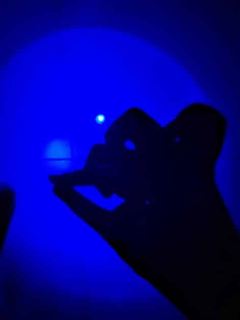 A glowing blue light emanating from a phone screen in a dark setting, casting a blue hue onto a wall, symbolizing artificial blue light sources.