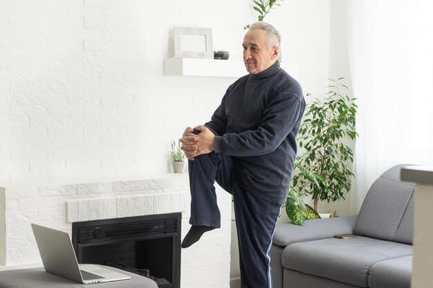 An elderly man gracefully performing a single-leg stand exercise while holding onto a chair for slight support in a bright, modern living room.