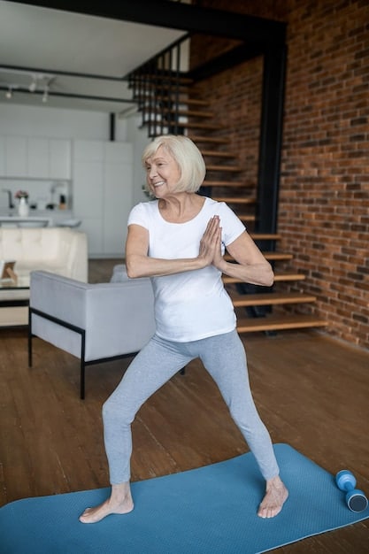 A senior woman smiling as she performs a standing march exercise, lifting one knee towards her chest while maintaining good posture, in a bright, inviting room.