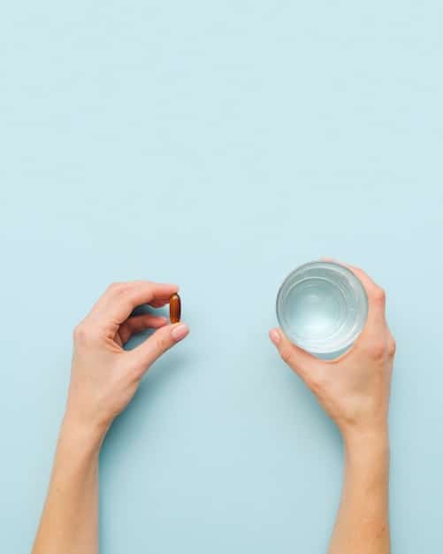 A person's hand holding a single probiotic capsule, with a blurred background of a daily calendar and a glass of water, emphasizing routine and healthy habits.