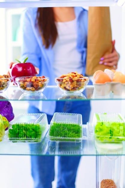 A person happily organizing prepped, colorful meals in glass containers into a refrigerator, showcasing efficient meal prep.