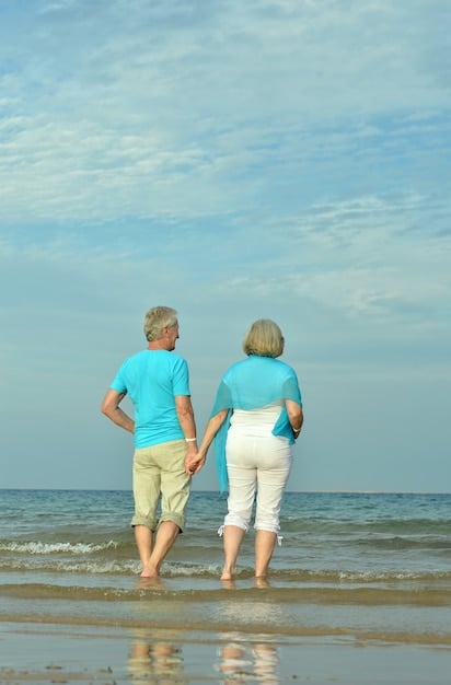 A serene elderly couple enjoying a gentle walk hand-in-hand along a coastal path, with the ocean waves in the background and a clear sky, symbolizing lifelong well-being and connection with nature.