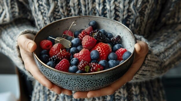 A person's hands holding a small bowl of mixed berries (blueberries, strawberries, raspberries) against a bright, natural light background.
