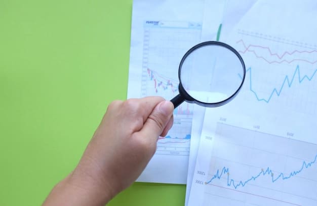 A close-up of a hand holding a magnifying glass over a graph showing rising inflation. The graph is displayed on a laptop screen in a brightly lit office. The words 